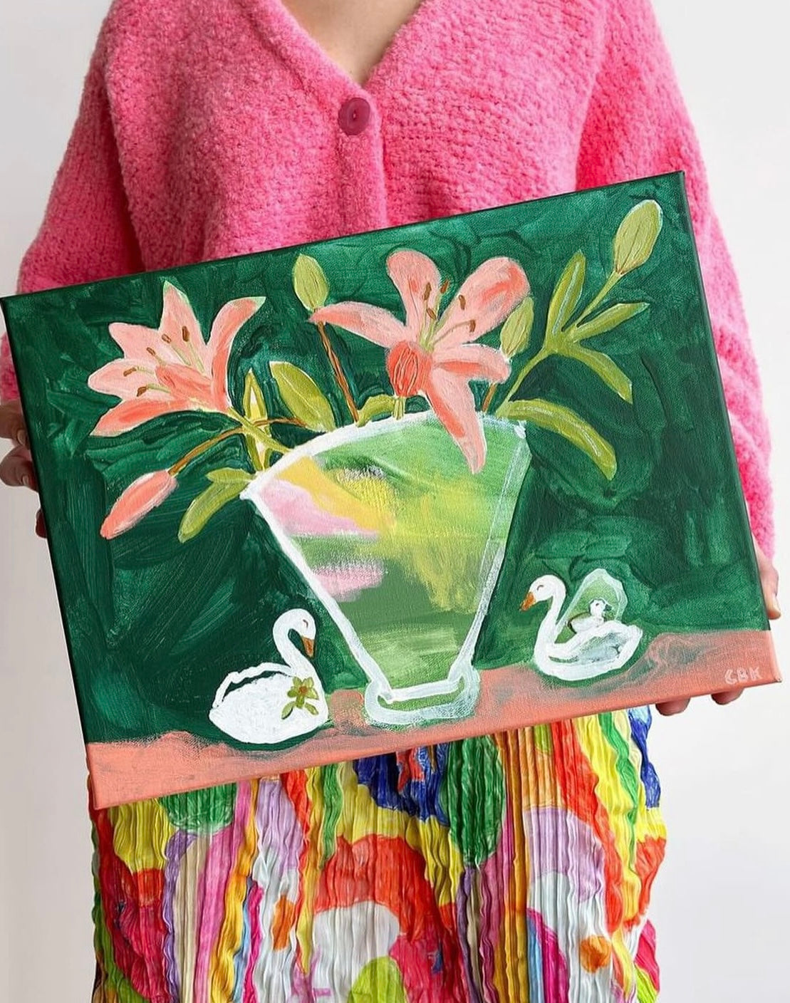 Crystals art being held up by someone wearing a pink cardigan. The art is most green with pink flowers in a vase