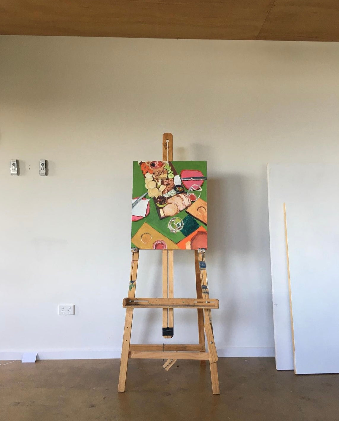 Art "Cider Tastings at Gurneys" On an easel in an empty room. Mostly green artwork featruing cheese and wine