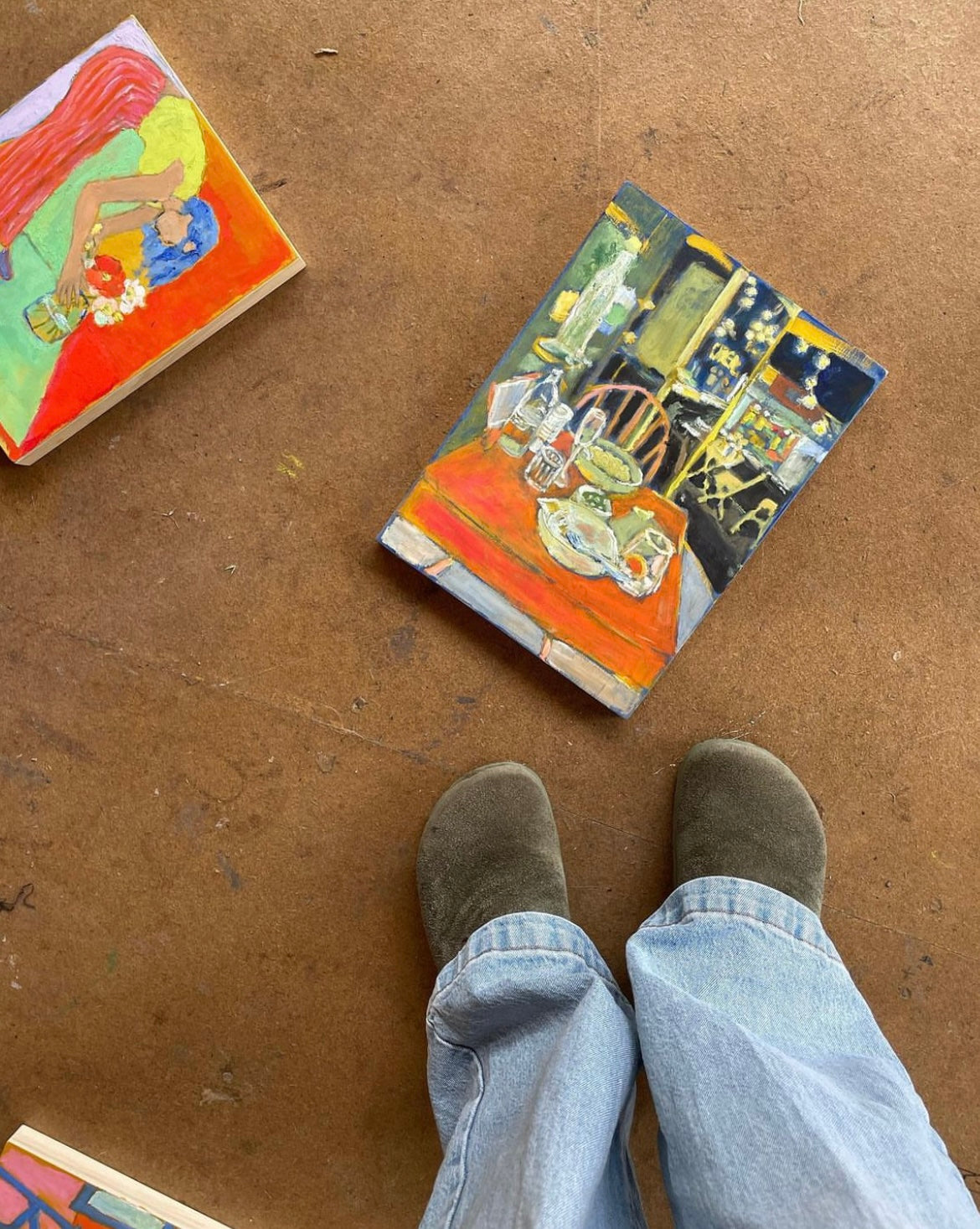 Paintings laying on the floor next to each other - one is a restaurant scene at night, the other is a woman putting flowers in a vase