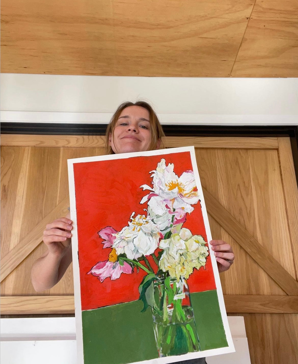 Jade holding a painting up of lowers in a vase on a red a green background